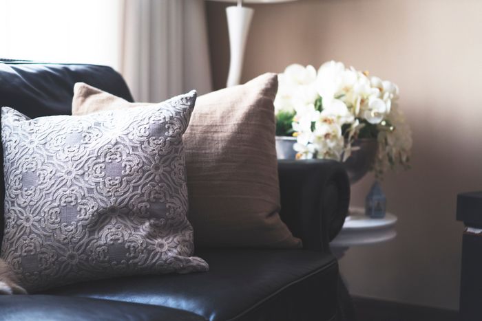 The arm of a leather couch with several soft pillows cushioning the corner.